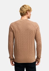 Beige kabelstrikket genser med strukturert mønster, ribbestrikkede mansjetter og nederkant. Har rund hals og raglanermer for bedre bevegelsesfrihet.