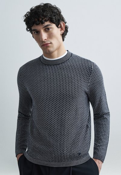 Pull en maille avec un motif structuré en noir et blanc, col rond, et manches longues avec poignets et ourlet côtelés.