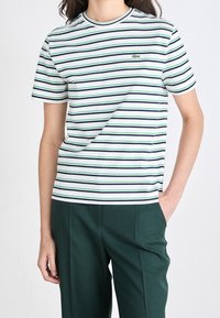 Randig t-shirt med horisontella linjer i marinblått, grönt och vitt, tillverkad av bomull med rundad hals och en liten broderad logotyp.