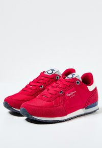 Sneaker rosse con una combinazione di materiali tessili e scamosciati, caratterizzate da un accento bianco, chiusura con lacci e dettaglio del logo sul lato.