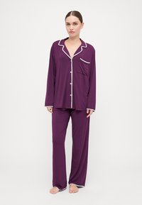 Set de pijama violet, cu mânecă lungă și detalii albe, având un buzunar pe partea de sus. Fabricat din material moale, cu croială lejeră și pantaloni drepti.