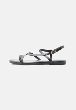 Black flat sandal with thin crisscross straps and a gold buckle ankle strap on a white background.