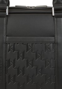 Czarna skórzana torba z teksturowanym geometrycznym wzorem, srebrnym okuciem i zamknięciem na zamek błyskawiczny, z płaską przednią kieszenią wyraźnie eksponowaną.