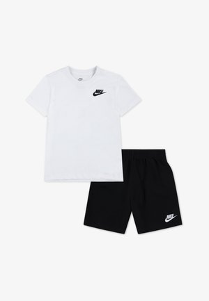 Camiseta blanca de algodón con el logo negro de Nike en el pecho, combinada con pantalones cortos negros de algodón que muestran un logo a juego cerca del dobladillo.