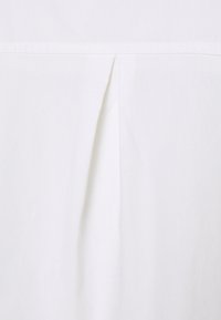 White fabric section with a centered inverted box pleat and horizontal seam above, showing subtle shadows and texture.