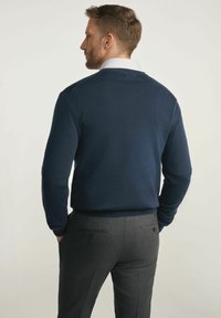 Granatowy, dziany sweter z okrągłym dekoltem, gładką fakturą i ściągaczami przy mankietach, w zestawie z szarymi, dopasowanymi spodniami z tylnymi kieszeniami.