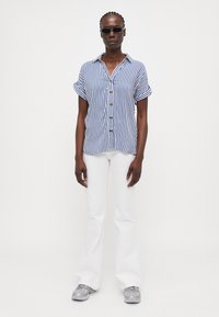 Gestreepte blauw-witte shirt met korte mouwen en een knoopsluiting aan de voorkant. Gecombineerd met witte flared broek en grijze sneakers. Eenvoudig, ontspannen ontwerp.