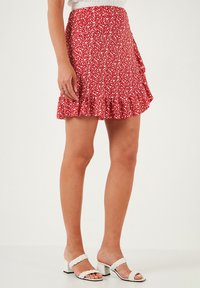 Rode bloemenpatroon rok met een geplooide zoom, gemaakt van lichtgewicht stof. Gecombineerd met witte sandalen met gevlochten straps en een getextureerde top.