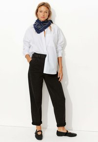 Chemise blanche à boutons, pantalon noir taille haute, écharpe marine à motifs et ballerines noires avec des accents cloutés. Tissu lisse et coupe décontractée.