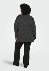 Tamno sivi pleteni džemper s opuštenim krojom, rebrastim rubom i teksturiranim rukavima. Uparen s crnim hlačama, gledano sa stražnje strane.