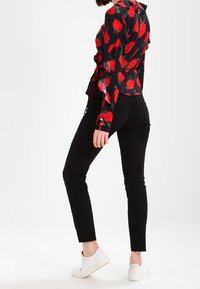 Langærmet sort skjorte med rødt blomstermønster, parret med sorte skinny jeans og hvide sneakers. Skjorten har en tætsiddende design og rynkede detaljer.