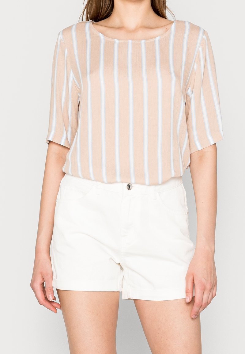 Beige kortärmad topp med ljusblå ränder, kombinerad med vita shorts, visar en avslappnad passform och mjuk textur.