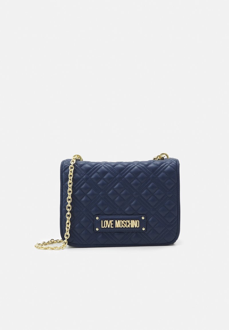 Sac à main matelassé bleu marine avec une bandoulière chaîne dorée, présentant une plaque logo dorée sur le devant et une forme rectangulaire avec des motifs en losange.