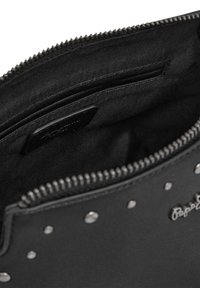 Intérieur d'un sac noir à fermeture éclair avec doublure en tissu, comportant une poche et des clous métalliques sur l'extérieur pour le détail.
