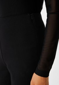 Czarny bodysuit z bezszwowym wzornictwem, z teksturowanej tkaniny, długimi przezroczystymi rękawami i dyskretnym zapięciem na zamek z boku.