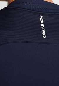 Marineblå Nike Pro-shirt med strukturerede horisontale linjer ved kraven, med "NIKE PRO" logo i hvidt tryk. Glat stoffinish.