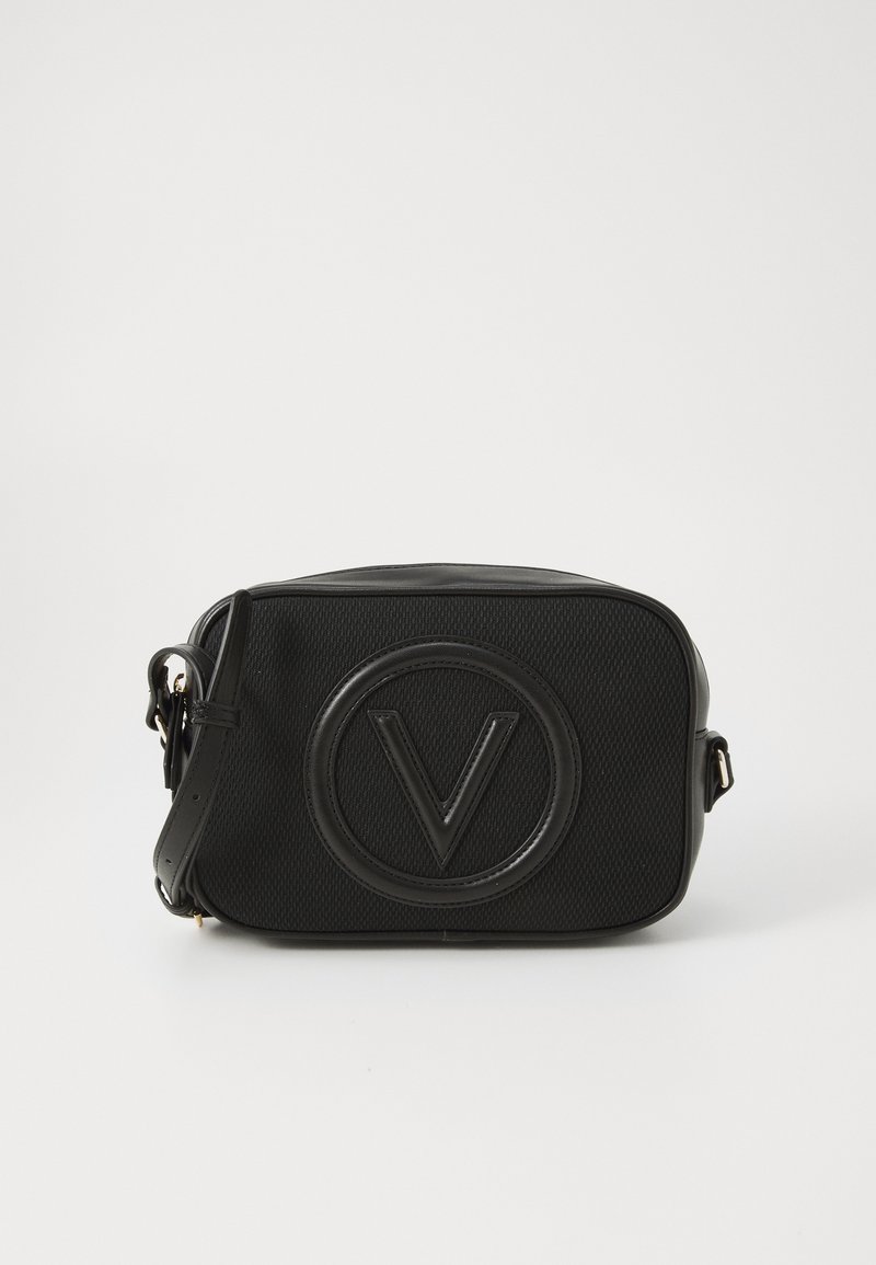Sac à bandoulière noir avec un tissu texturé, un logo circulaire en relief, une forme rectangulaire et une sangle réglable.