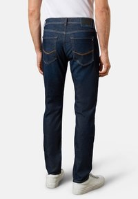 Dunkelblaue Denim-Jeans im Slim-Fit, mit gesteppten Gesäßtaschen, einem schwarzen Etikett am Bund und einer glatten, strukturierten Oberfläche.