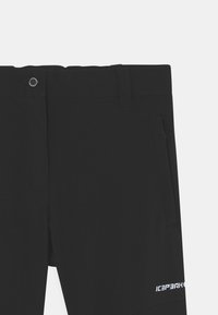 Sorte shorts laget av et glatt, elastisk stoff; har en frontlomme, beltehemper og en logo i hvitt nederst til høyre.