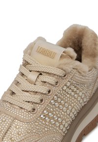 Sneaker beige con rivestimento in peluche, caratterizzato da strass decorativi e tessuto testurizzato. Lacci intrecciati, suola in gomma e dettaglio del logo.