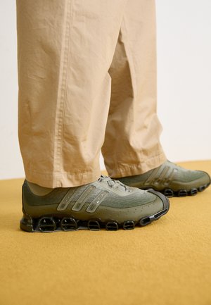 Grønne atletiske sko med mesh- og syntetisk overdel, teksturerede detaljer og en karakteristisk sort sål med cirkulære støtdæmpende elementer.