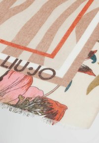 Bufanda suave y estampada con tonos tierra y motivos florales, con bordes con flecos y un logo de la marca. Con forma rectangular y tejido ligero.