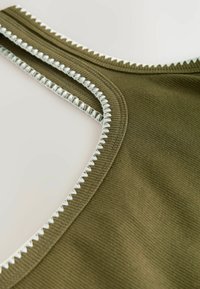 Material ribbed de culoare verde măsliniu cu un decolteu larg și rotund. Cusătura zigzag albă accentuează marginile. Textură fină cu o formă structurată.