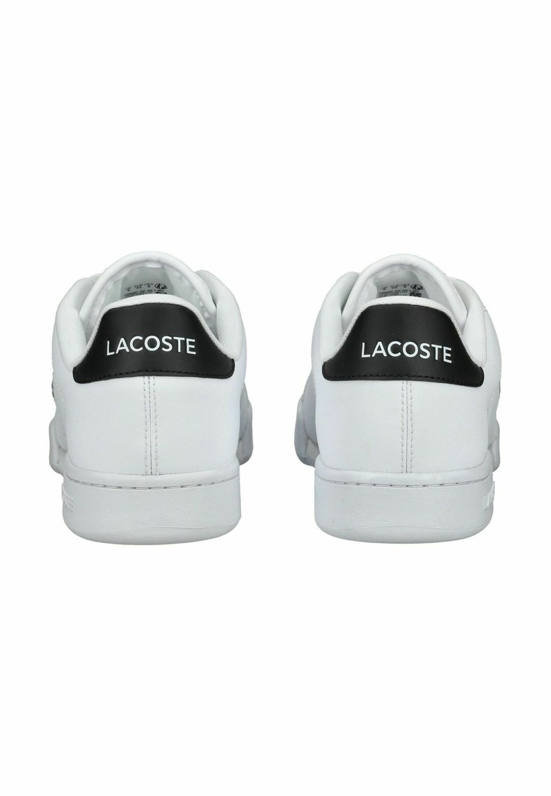 Baskets en cuir blanc avec un empiècement de talon noir, arborant le logo "LACOSTE". Texture lisse, design minimaliste et fermeture à lacets.