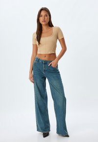 Crop top beige a coste con maniche corte, abbinato a jeans a gamba larga blu e stivali neri con tacco alla caviglia. Tessuto morbido e vestibilità casual.