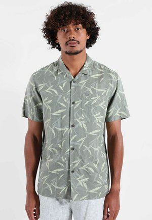 Chemise à manches courtes boutonnée en vert avec un motif de feuilles, fabriquée en tissu léger, arborant une poche poitrine et des boutons marron.