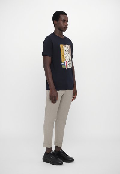 T-shirt bleu marine avec un graphique de chien cartoon et du texte, associé à un pantalon beige clair et des baskets noires. Coupe simple, en coton.