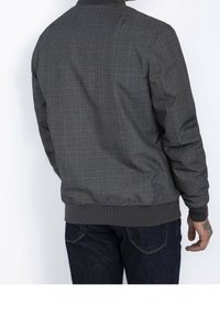 Blouson aviateur gris à motifs avec col et poignets côtelés, présentant une finition texturée et un design à carreaux subtil.