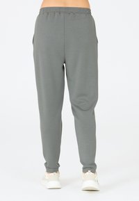 Lichtgrijze joggers met een elastische tailleband, zijzakken en een taps toelopende pasvorm. Gemaakt van een zachte, rekbare stof. Gecombineerd met witte sneakers.