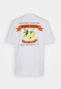 Bílá bavlněná tričko s barevným potiskem citronu, oranžová stužka s nápisem "KARL KANI" a textem uvádějícím datum a místo založení.