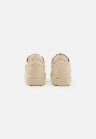 Scarpe slip-on beige con una consistenza liscia e un retro arrotondato. Presentano un logo discreto sul tallone e semplici dettagli di cucitura.