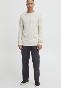 Suéter largo de manga larga de color beige claro con escote redondo, combinado con pantalones gris oscuro y zapatillas negras. Diseño sencillo y corte relajado.