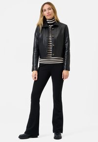 Zwarte leren cropped jack met knoopsluiting, gecombineerd met een zwart-wit gestreepte coltrui, zwarte flared broeken en stevige zwarte schoenen.