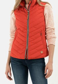 Czerwona pikowana kamizelka z wysokim kołnierzem, zamkiem błyskawicznym z przodu i dwoma bocznymi kieszeniami; wykonana z lekkiego, ocieplanego materiału.