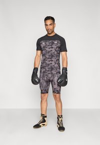 Lühikeste varrukatega hall kamuflaažspordisärk, millele sobitatud kompressioonpüksid, mustad poksikindad ning kõrgete mustade ja beežide tossudega.