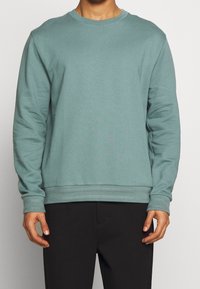 Hellblauer Crewneck-Sweatshirt mit langen Ärmeln, gerippten Bündchen und Saum. Hergestellt aus weichem Material, mit lässiger Passform und minimalistischem Design.