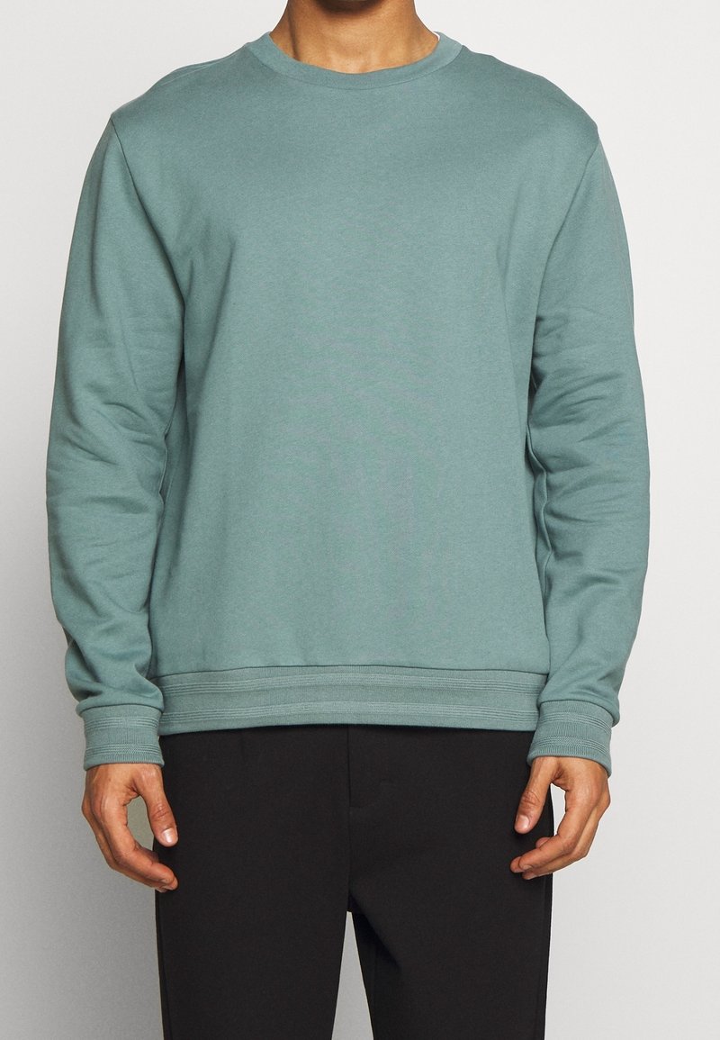 Hellblauer Crewneck-Sweatshirt mit langen Ärmeln, gerippten Bündchen und Saum. Hergestellt aus weichem Material, mit lässiger Passform und minimalistischem Design.