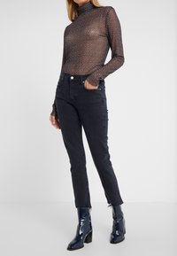 Haut à col roulé à manches longues en tissu transparent avec un motif floral sombre, associé à un jean taille haute foncé et des bottes brillantes montant jusqu'aux genoux.