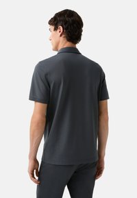 Mørkegrå polo-shirt med korte �ærmer og krave. Har en glat tekstur, minimale detaljer og en skræddersyet pasform, vist fra bagsiden.