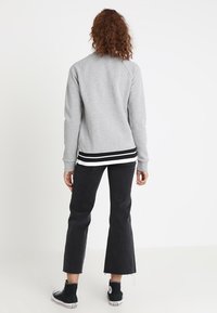 Szary sweatshirt z raglanowymi rękawami, z czarno-białym paskiem u dołu. W zestawie z czarnymi, wąskimi spodniami i wysokimi trampkami.