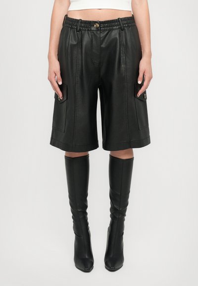 Zwarte leren shorts met een elastische tailleband, zijzakken en een gestructureerd ontwerp. Dressed met strakke zwarte kniehoge laarzen. Matte textuur.