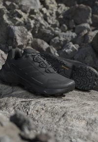 Coppia di scarpe da trail running nere con suola strutturata su superficie rocciosa, progettate per uso esterno e terreni accidentati.