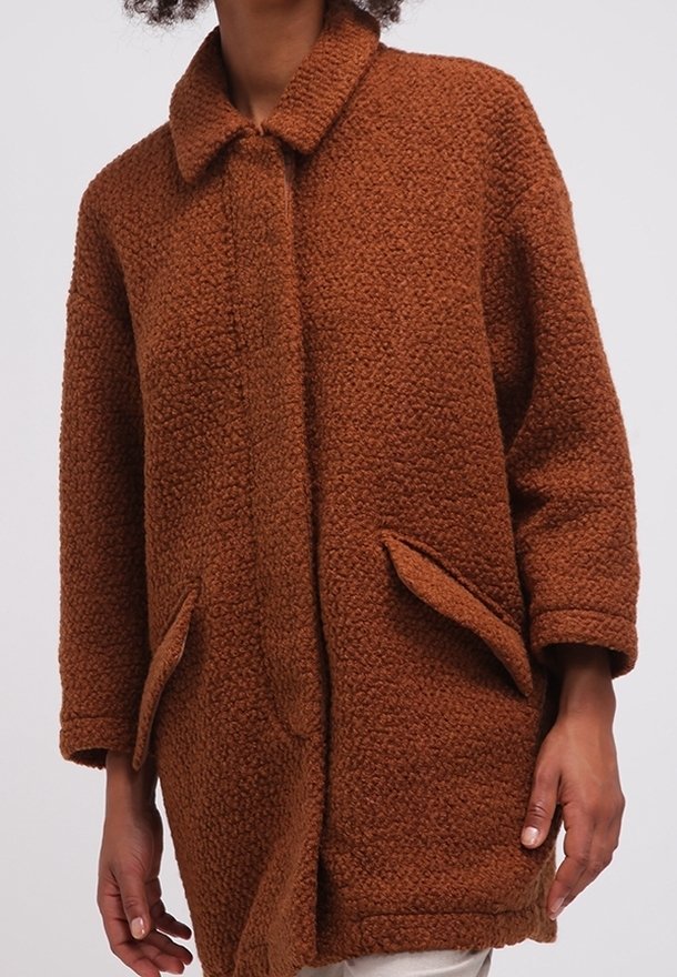 Brun texturerad rock med krage, knappstängning framtill och sidofickor. Tillverkad av ett fluffigt material, med en avslappnad passform.