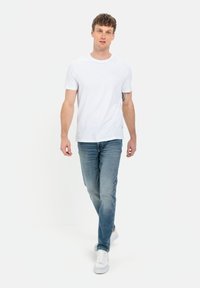 Hvid crew-neck t-shirt kombineret med lyseblå jeans og hvide sneakers. Tøjet har et simpelt, afslappet design med minimale detaljer.