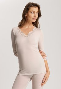 Light pink long-sleeve top with a v-neck, featuring lace trim at the collar and cuffs, made from ribbed fabric. Soft texture, fitted design.