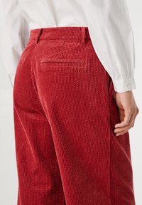 Sarkana kordura bikses ar vertikālu ribotu tekstūru, ar aizmugurējo kabatu un pieguļošu piegriezumu. Saskaņotas ar baltu krekli ar pogu.